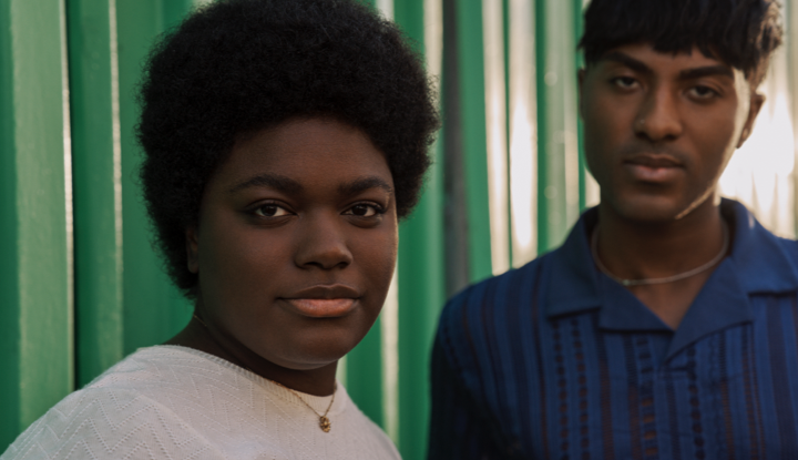 Two people in front of a green wall.